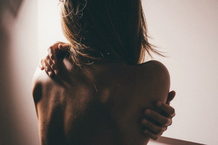 A woman holding her bare, glowing shoulders in soft, warm light