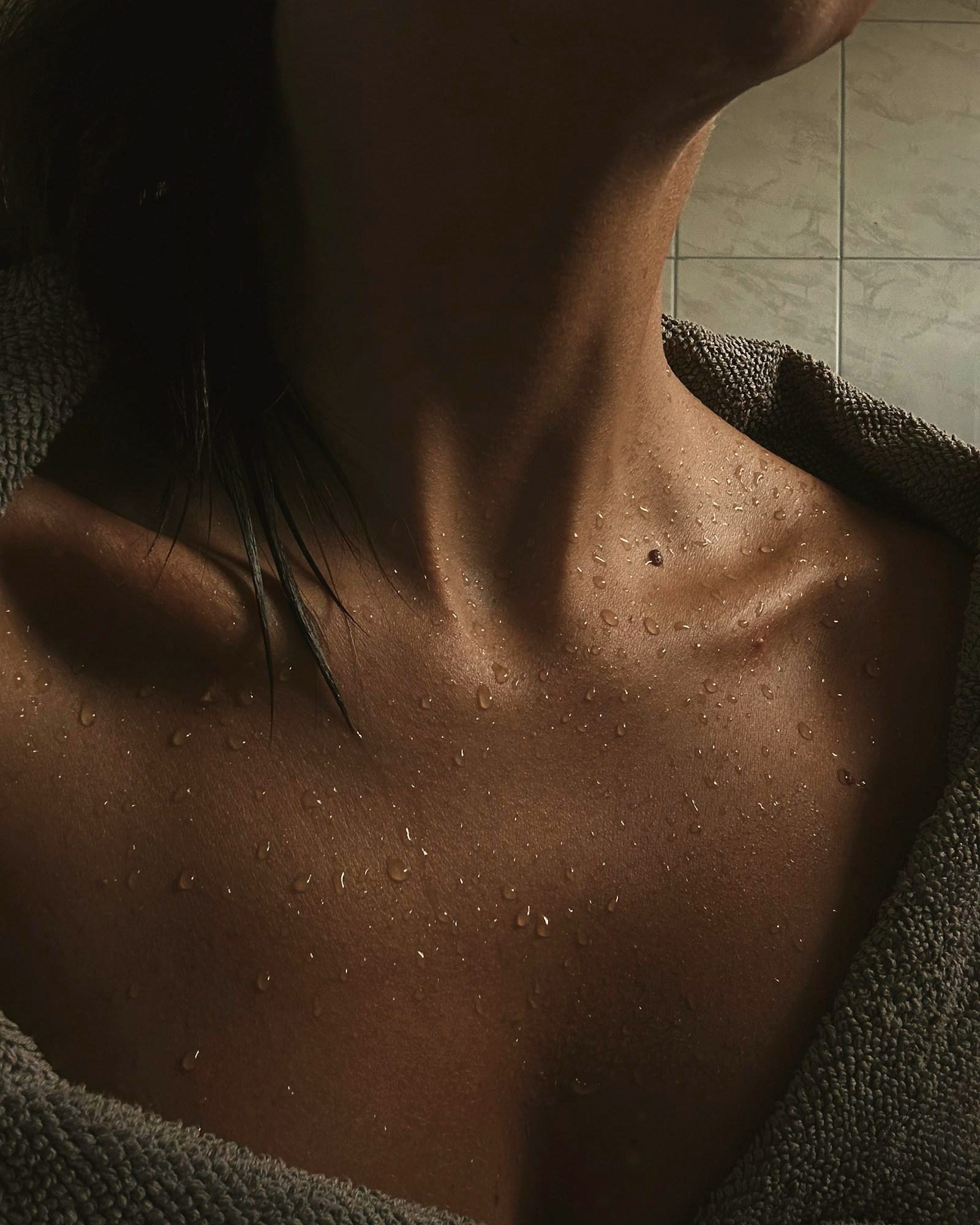 Close-up of glowing, bronzed skin at the collarbone, wrapped in a soft towel